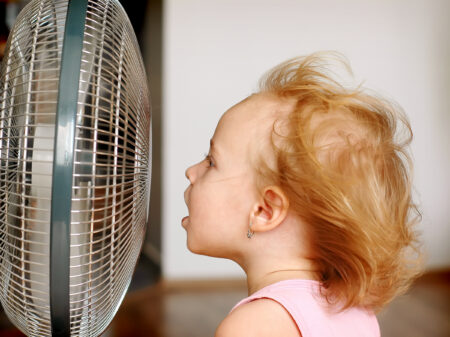 A little girl standing in front of fan